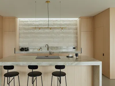 A modern kitchen with a marble countertop, wooden cabinets, and black stools.