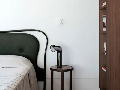 A minimalist bedroom featuring a black headboard bed, a wooden bedside table with a black lamp, and a wooden bookshelf.