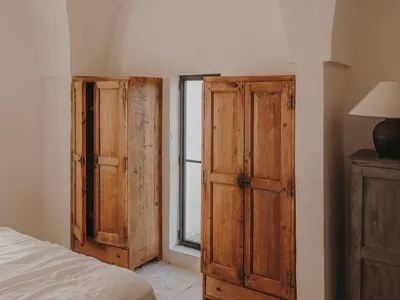 A minimalist bedroom with wooden furniture, white bedding, and a window with a view of the outdoors.