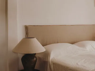 A minimalist bedroom featuring a bed with beige linen bedding and a ceramic lamp on a small side table.