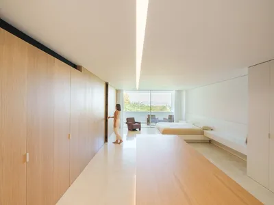 A modern minimalist bedroom featuring wooden flooring and a glass wall with a view.