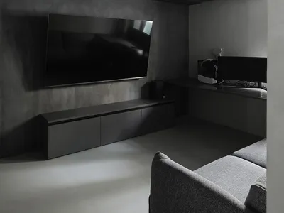 Modern industrial-style living room with concrete walls and floor, featuring a flat-screen TV and grey upholstered furniture.