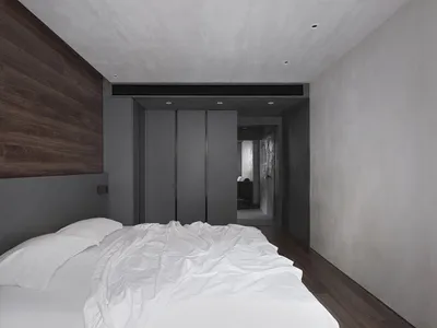 A minimalist bedroom with a concrete wall and a creased white duvet on the bed.