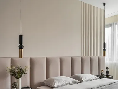 A minimalist bedroom with a beige fabric headboard and a grey bedspread, featuring modern pendant lights and nightstands with