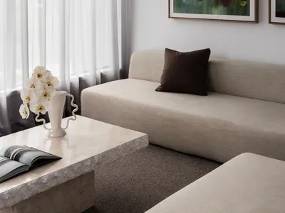 Modern minimalist living room with neutral tones, upholstered furniture, and abstract artwork.