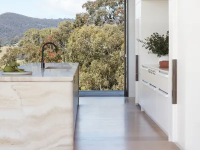 極簡風格的廚房，設有大理石中島，並有通往戶外的開門，映入山景與綠意。