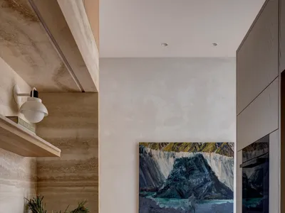 A modern minimalist kitchen with concrete walls and wood cabinets, featuring a painting of a mountain landscape.