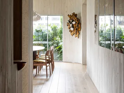 A modern restaurant corridor featuring wooden walls and floor, glass walls, and a wooden hanging decoration.