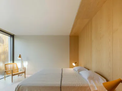 Modern minimalist bedroom with wooden walls and furniture, featuring a bed with a wooden headboard and matching bedside table