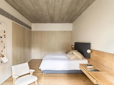 Modern minimalist bedroom with a white texture on the floor, walls, and furniture, featuring a bed with white bedding and a w