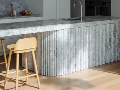 Modern kitchen interior with marble island and stools.