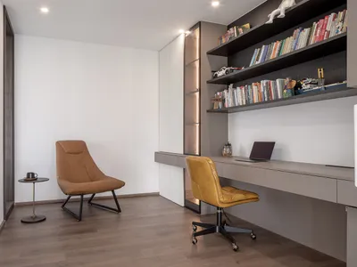 A modern home office with a wooden floor, brown leather chairs, and a built-in bookshelf.