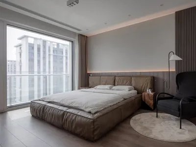 A minimalist bedroom featuring a large bed made of leather, a black armchair, and a round rug.