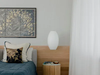 A minimalist bedroom featuring a bed with cotton linens and wood headboard, alongside a glass bedside table with a pendant la