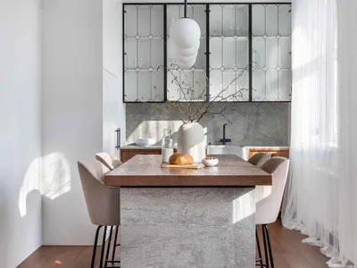 Modern kitchen with wooden dining table and concrete island, featuring a hanging pendant light and beige upholstered chairs.