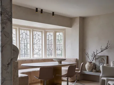 Contemporary living room featuring a wooden dining table, chairs, and sofa, with a white vase and a window with stained glass