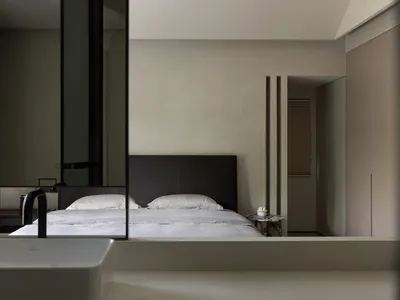 A minimalist bedroom with a white bed, black headboard, and textured walls.