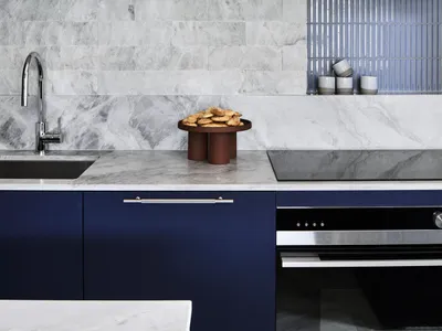 現代廚房配有大理石檯面與下方藍色櫃體，搭配大理石背板、架上藍色杯子，以及