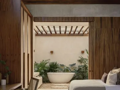 A modern bathroom with a concrete floor and wooden planks, featuring a bathtub surrounded by lush green plants.