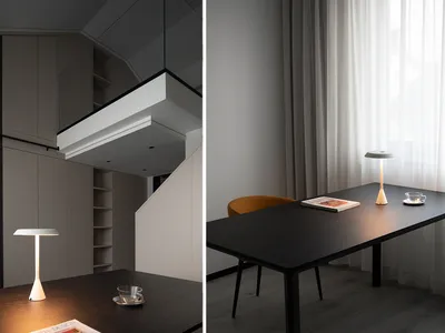 A modern home office setup featuring a wooden desk and chair, with curtains and a lamp illuminating the space.