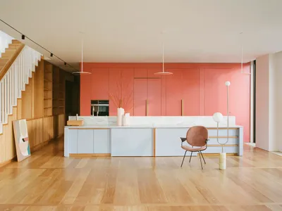 Modern kitchen with white marble countertops, brown wooden cabinets, and a plastic chair.