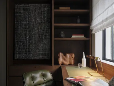 A minimalist home office featuring custom shelving, a green leather chair, and a desk with a table lamp, books, and a glass c