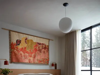 Minimalist bedroom featuring a wooden bed with white bedding, large tapestry, and a wooden bench.