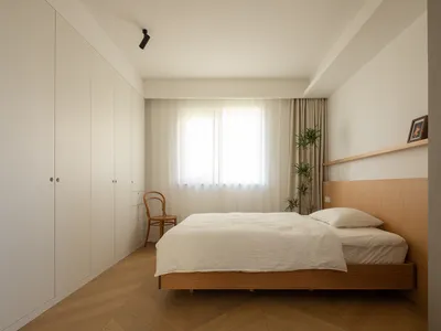 A modern minimalist bedroom featuring a wooden bed and furniture, with a large window and a white wall.