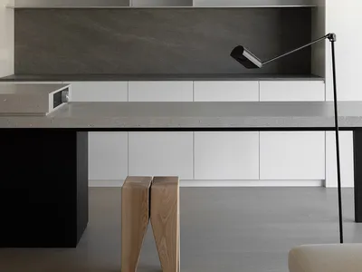 A modern minimalist kitchen with white cabinets, a concrete countertop, and wooden stools.