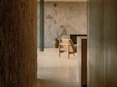 A minimalist living room with concrete walls, a wooden armchair, and a vase with green branches.