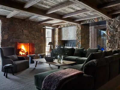 A cozy living room with wooden and stone elements, featuring a comfortable sofa, chairs, and a warm fireplace.