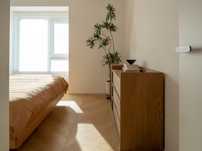 A minimalist bedroom featuring a bed with wood frame and beige bedding, surrounded by concrete walls and a wooden dresser.
