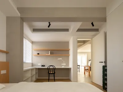 A minimalist bedroom with wooden shelves, a black chair, and a white desk.