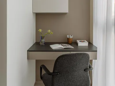 A minimalist home office featuring a beige-grey desk with a wooden drawer, a grey upholstered chair, and a beige-grey cabinet