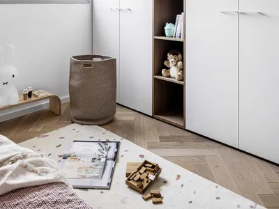 Minimalist bedroom with white walls, wooden furniture, and a large window allowing natural light to enter.