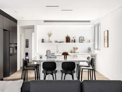 A modern kitchen featuring a black marble island with black chairs and wooden flooring, surrounded by white walls and black c