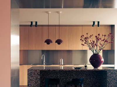 A modern minimalist kitchen featuring granite countertops, wooden cabinets, and black stools next to a vase with flowers.