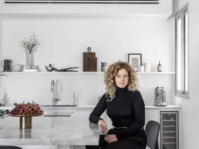 A minimalist kitchen featuring a marble countertop with a woman sitting on a stool.