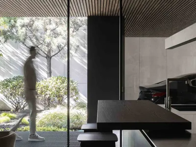 A modern kitchen with a wooden island counter, large windows, and a black stool.