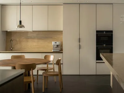 A modern kitchen with minimalist design featuring concrete countertops, wooden chairs, and stainless steel appliances.