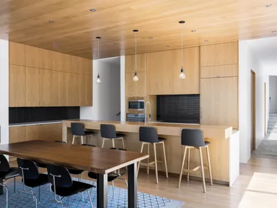 Modern kitchen with light wood cabinets, metal stools, and a dining table.