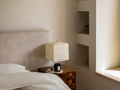 A minimalist bedroom with neutral-colored walls, bed, and shelves.