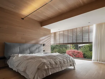 Modern bedroom with wooden walls, ceiling, and floor, featuring a comfortable bed with a grey cushioned headboard and neutral