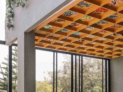 A cafe interior design featuring a wooden ceiling adorned with colorful floral patterns, potted plants, and a table with stoo