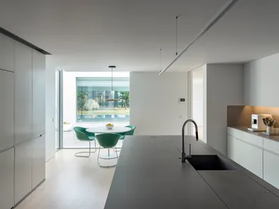 Modern minimalist kitchen with concrete countertops, white cabinets, and green chairs.