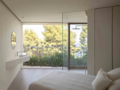 A minimalist bedroom with glass walls and a view of greenery.