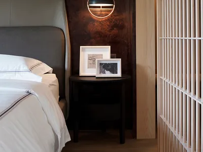 A minimalist bedroom featuring dark wood elements and a white bed with a gray headboard.