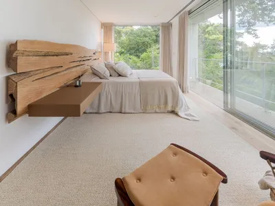 A minimalist bedroom featuring a wooden headboard, a carpeted floor, and a bed with pillows, situated in front of a large win