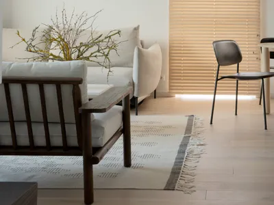 Minimalist living room with wooden flooring, white walls, and a window with wooden blinds, showcasing budget-friendly design