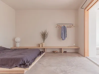 A minimalist bedroom with a concrete floor and a low wooden bed platform.